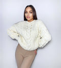 May include: A white cable knit sweater with a chunky texture. The sweater has a round neckline and long sleeves.