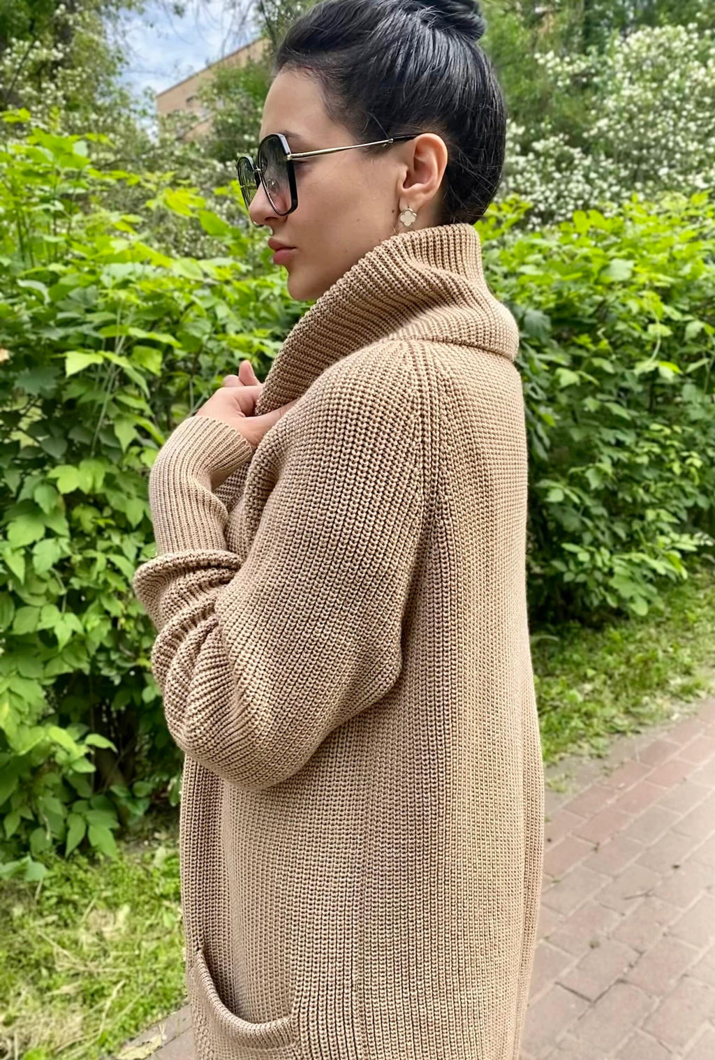May include: A long-sleeved, beige cardigan with a high collar and a ribbed knit texture. The cardigan has two pockets on the front.