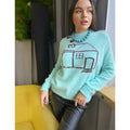 May include: A light blue fuzzy sweater with a brown cartoon house design. The sweater has a round neck and long sleeves.