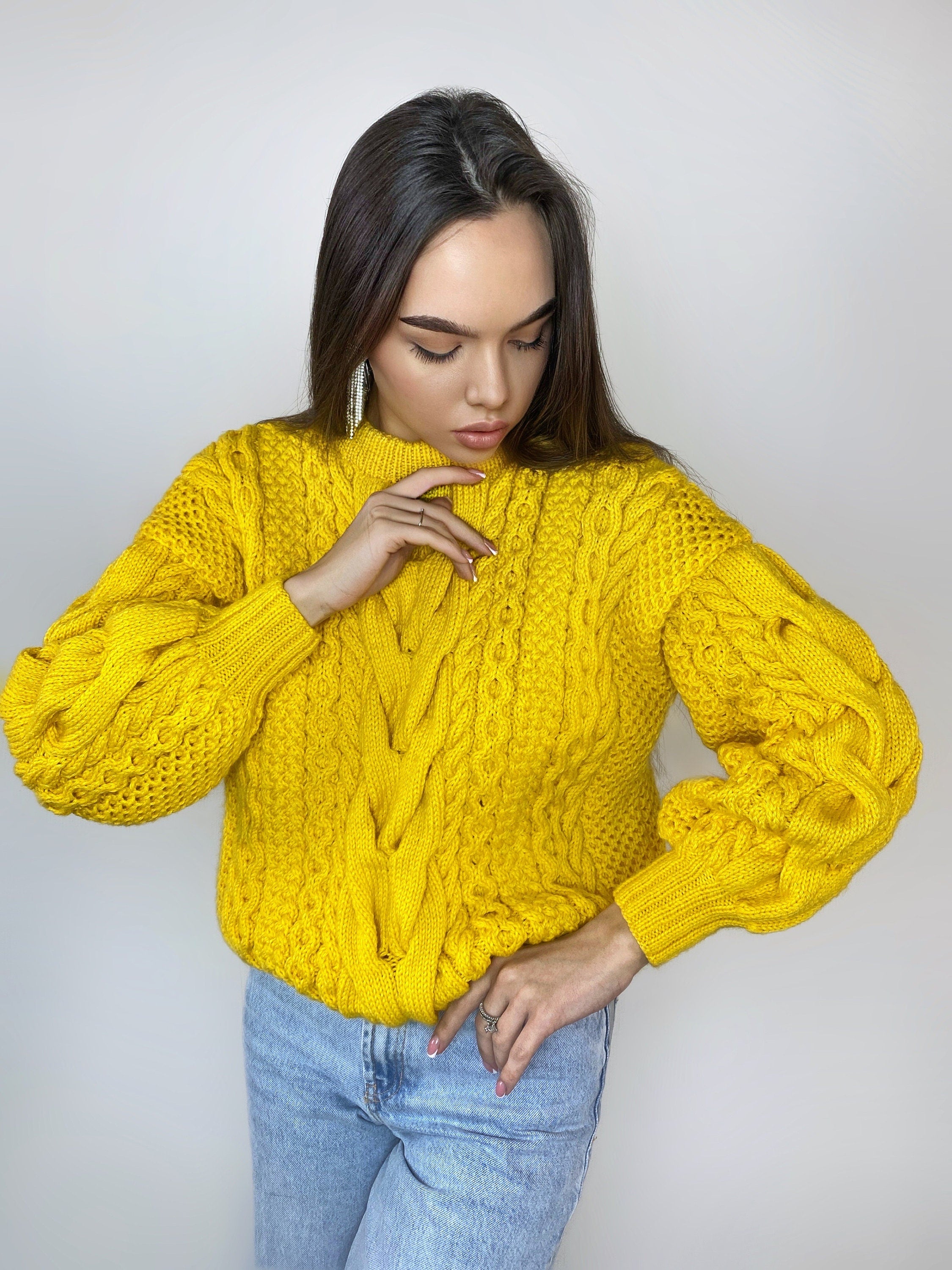 May include: A yellow cable knit sweater with a round neckline and long sleeves. The sweater has a loose fit and a textured pattern.