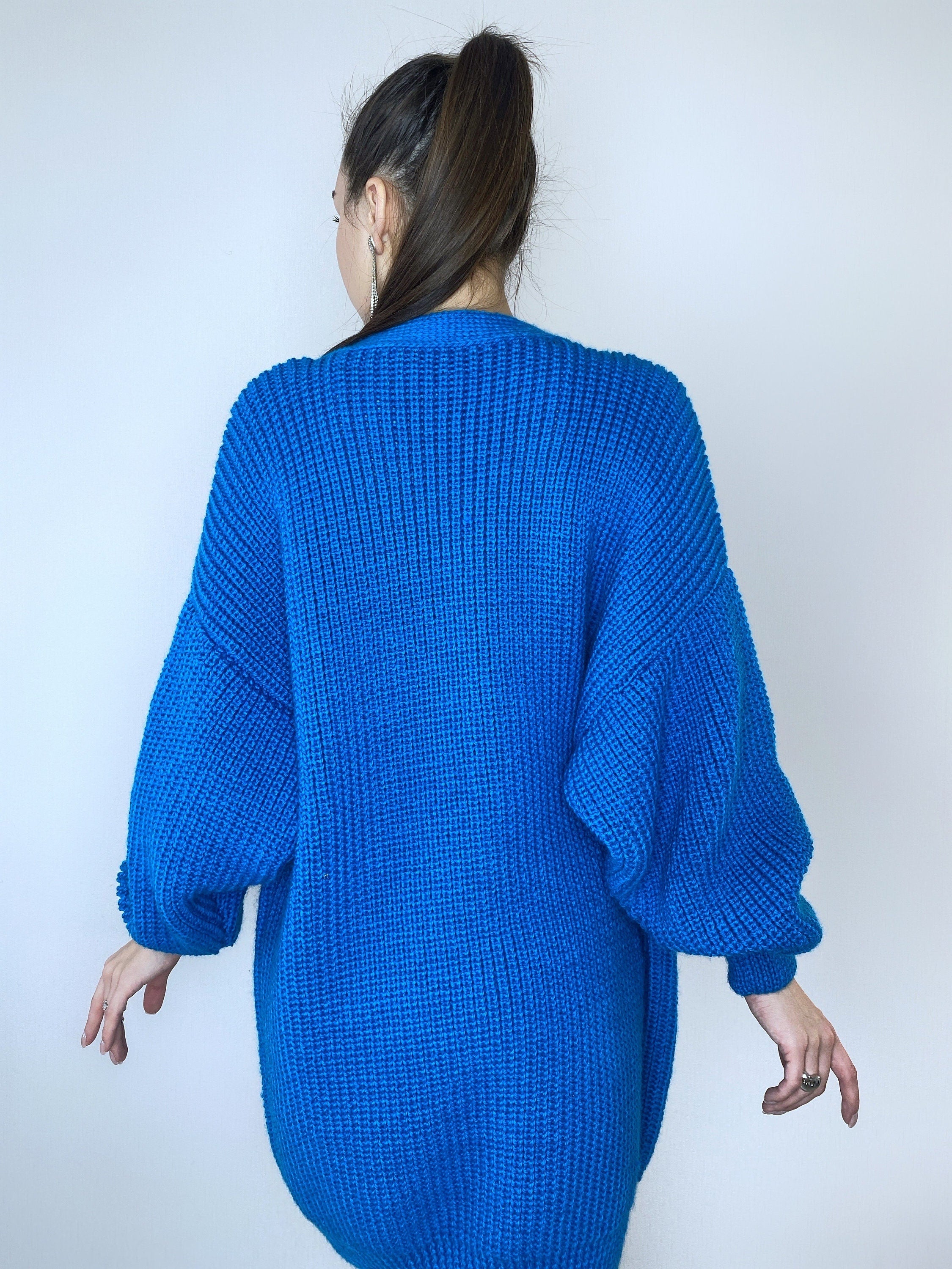 May include: A bright blue knitted cardigan with long sleeves and a relaxed fit.