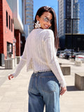 May include: A white cable-knit sweater with long sleeves and a lace trim, paired with blue denim jeans. The sweater has a split back design. The model is wearing sunglasses and large white flower earrings.