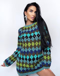 May include: A long-sleeved, crochet dress featuring a geometric pattern in shades of green, blue, and black. The dress has a crew neck and a turquoise trim at the neckline and hem. The dress is made of a soft, comfortable material.