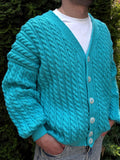 May include: A turquoise cable-knit cardigan with a V-neck and button closure. The sweater features a textured pattern and long sleeves. The buttons are white. The person is wearing a white t-shirt underneath.