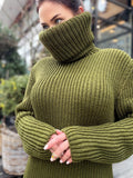 May include: Olive green turtleneck sweater with ribbed knit texture. The sweater features a high, oversized collar and long sleeves. The knitwear is a solid color, and the sleeves are cuffed at the wrists.